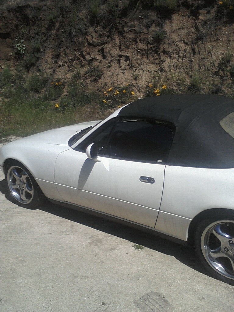 White convertible roadster with black soft top, side view on gravel by dirt bank