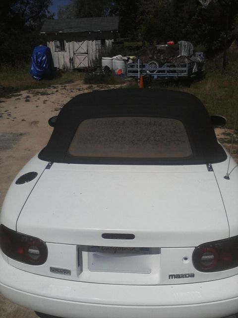 1968 Ford Mustang - Rear view of a white Mazda convertible with the black soft top raised, smoked round taillights, blacked-out badging, a California plate and…
