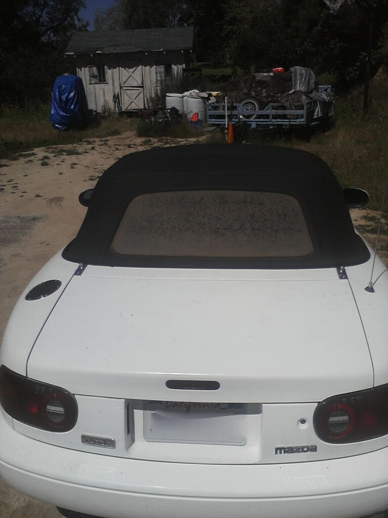 Rear of white Mazda convertible with black soft top and smoked taillights on dirt lot