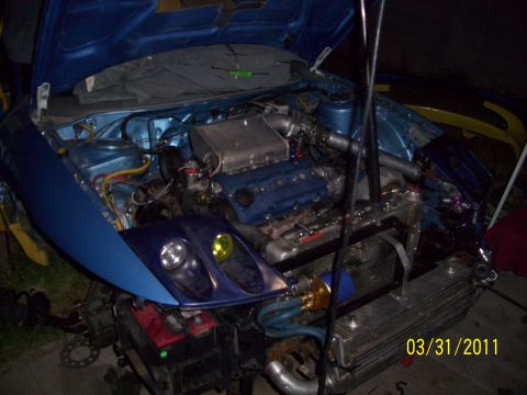 1995 Ford Probe - The engine bay of a blue car is exposed, revealing custom modifications and parts.