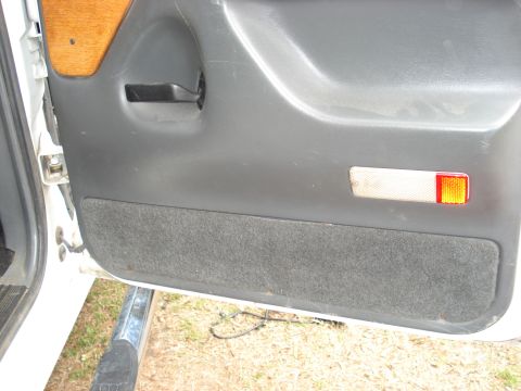 1992 Ford C-350 (Centurion Conversions) - Interior view of a vehicle door panel, showing the handle, wood trim, and a reflector.