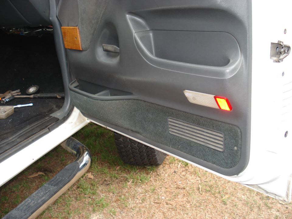 Gray rear door panel of white truck with speaker grille, storage tray and red reflector