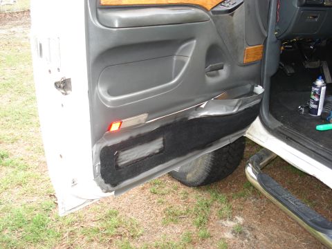 1992 Ford C-350 (Centurion Conversions) - Open driver's door of a white Ford truck with the lower door panel carpet partially peeled back and masked off with tape, exposing the gray…