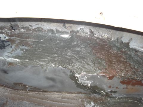 1992 Ford C-350 (Centurion Conversions) - Extreme close-up of bodywork in progress on a curved panel edge, showing bare ground-down sheet metal with smeared gray body filler over pa…