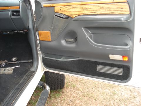 1992 Ford C-350 (Centurion Conversions) - Open driver's door of a white Ford truck showing the gray door panel with woodgrain trim strips, molded armrest and pull cup, amber reflect…