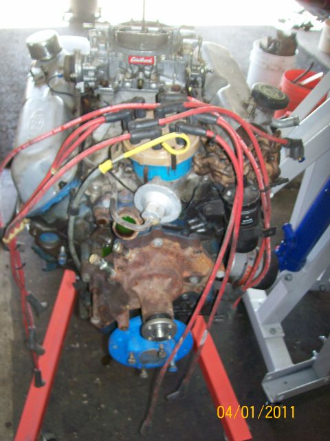 1970 Ford Bronco - Engine assembly with Edelbrock carburetor and red spark plug wires, mounted on a stand for service.