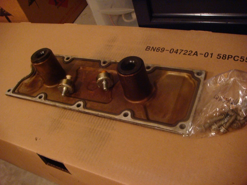 Engine valve cover with two sensors and a bag of bolts on a cardboard box