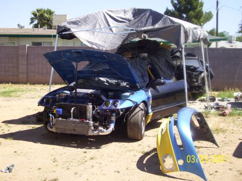 1995 Ford Probe - A blue car is disassembled outdoors under a tarp, with its hood open and various parts scattered around.