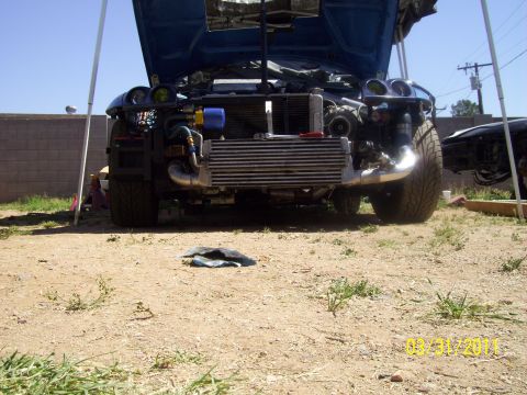 1995 Ford Probe - Front end of a blue car is disassembled, revealing the intercooler and engine components. Another vehicle is partially visible to the right.
