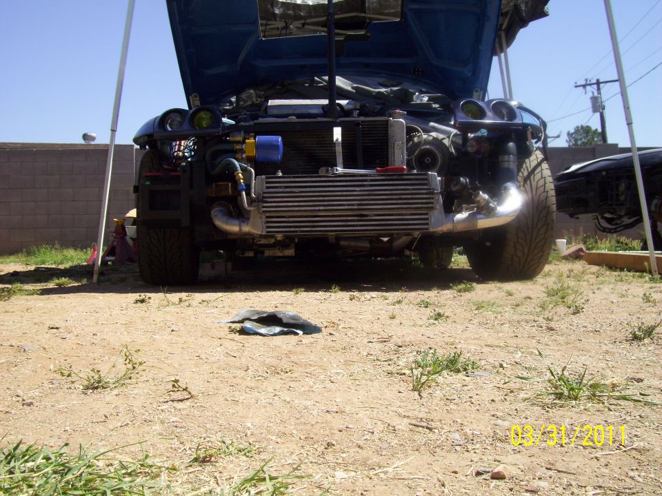 Blue car front end disassembled, intercooler exposed. Another car visible to the right