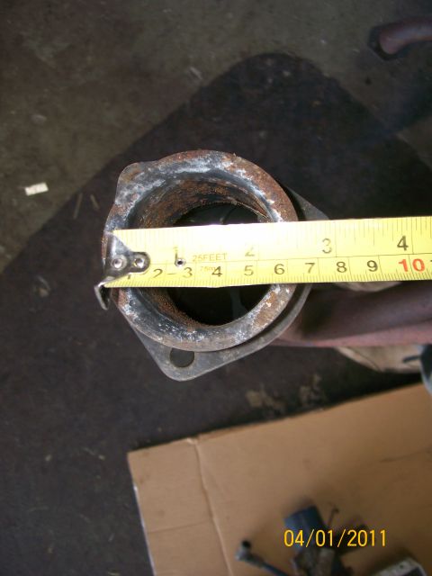 1970 Ford Bronco - A tape measure is used to show the diameter of a rusty exhaust pipe with a flange.