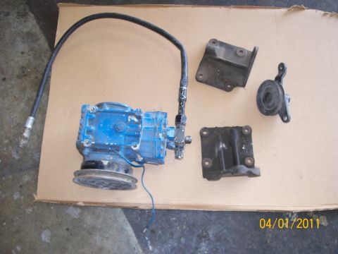 1970 Ford Bronco - A blue air conditioning compressor and associated parts are laid out on a piece of cardboard.