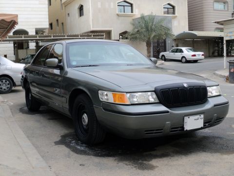 2001 Mercury Grand Marquis - A gray Mercury Grand Marquis is parked on a street in front of a building, with another car in the background.