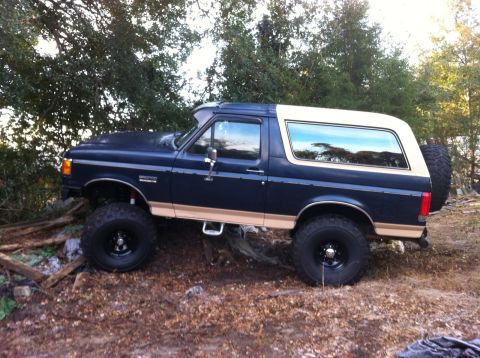 1990 Ford Bronco - This lifted Ford Bronco is shown in a side profile, parked outdoors on a dirt and debris-covered surface.