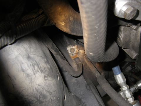 1990 Ford Bronco - Close-up view of hoses and metal parts within an engine bay, showing a rusted bolt securing a hose bracket.