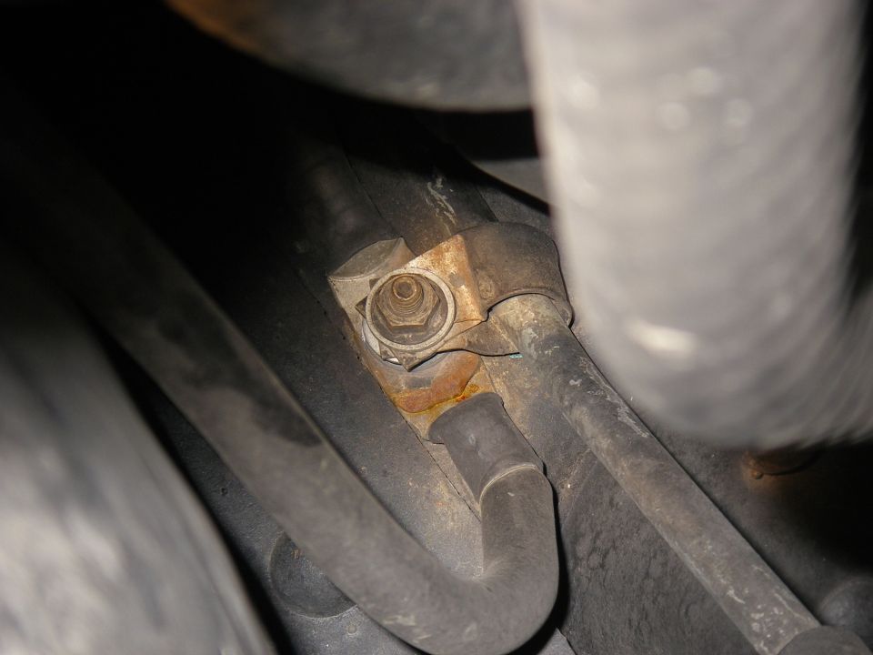 rusted metal bracket holding a bolt, with black hoses nearby