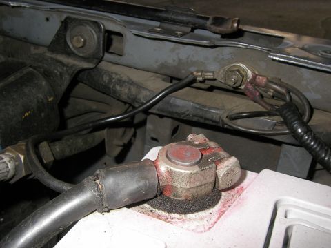 1990 Ford Bronco - Close-up of a battery terminal clamp on a white-cased battery, showing white and pink corrosion powder around the post and a thick cable wi…