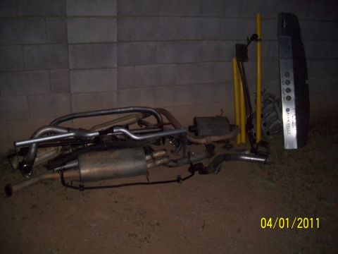 1995 Ford Probe - Various exhaust system components are laid out on the ground next to some yellow poles and a silver bumper.