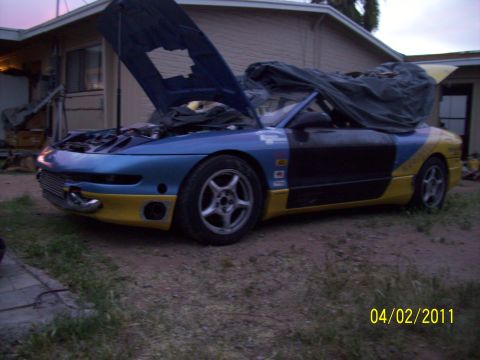 1995 Ford Probe - A customized sports car with its hood open and part of the interior covered sits in a yard.