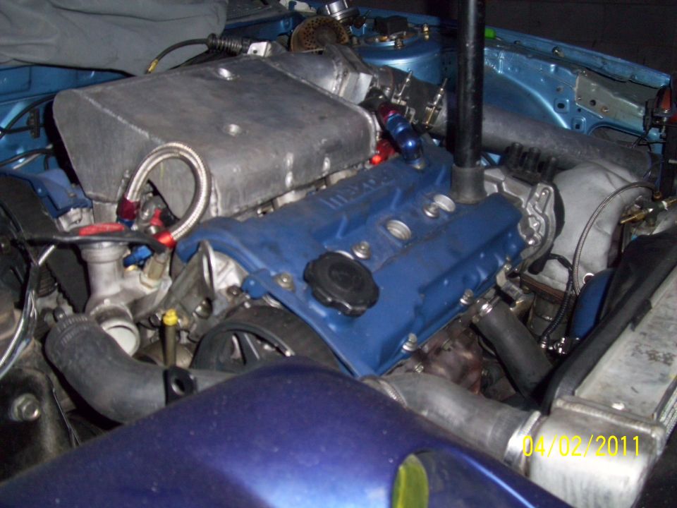 Engine bay with blue valve cover and large silver intake manifold. Some hoses and wiring are visible