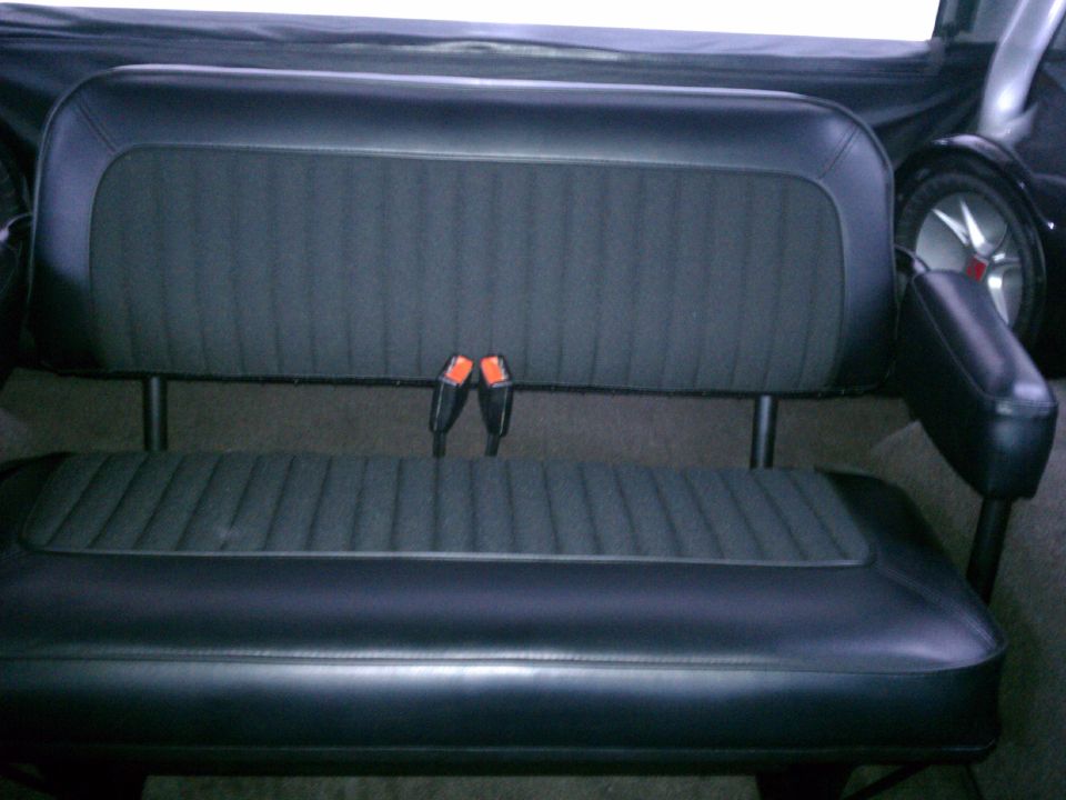 Black vinyl bench seat with gray cloth inserts, seat belt buckles, and side-mounted speakers inside a 1975 Ford Bronco