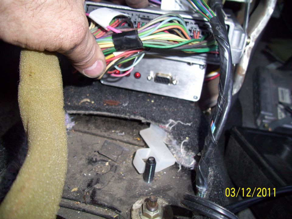Close-up of a car's wiring harness and electronic control module, with a hand holding wires