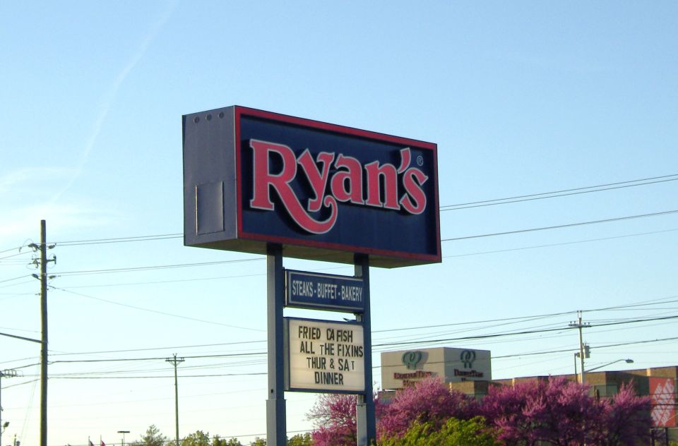 Ryan's restaurant sign with 'Steaks, Buffet, Bakery' and 'Fried Catfish All The Fixins Thur & Sat Dinner' below. Other buildings and trees in background