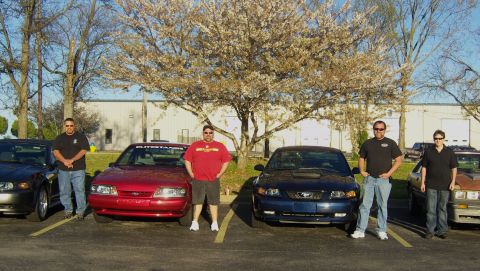 2007 Ford Mustang - Four people pose with four Ford Mustangs, including a red 1994 model.