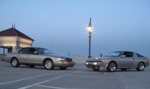 2000 Mercury Grand Marquis - Two cars, a silver coupe and a tan sedan, are parked on pavement under a dusky sky.