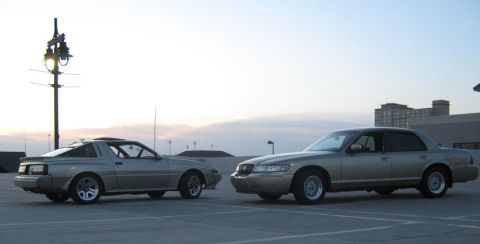 2000 Mercury Grand Marquis - A 2000 Mercury Grand Marquis is parked next to a silver coupe under a cloudy sky.