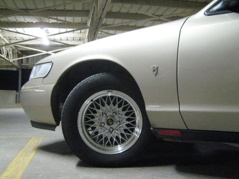 2000 Mercury Grand Marquis - Front quarter panel and wheel of a tan 2000 Mercury Grand Marquis, distinctive mesh alloy wheels and a fender emblem.