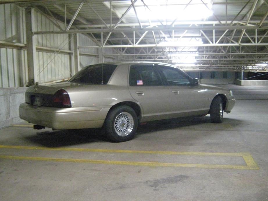 Tan 2000 Mercury Grand Marquis parked in a garage. It has aftermarket wheels and tinted windows