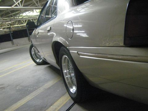2000 Mercury Grand Marquis - Rear quarter panel view of a gold Mercury Grand Marquis with custom wire wheels and a cougar emblem.
