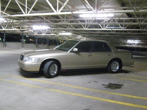 2000 Mercury Grand Marquis - A gold sedan is parked in a multi-level parking garage under fluorescent lights.