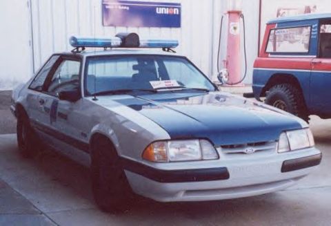 1991 Ford LTD Crown Victoria - A two-tone police car, likely a Ford Mustang, is parked next to a red and blue SUV.