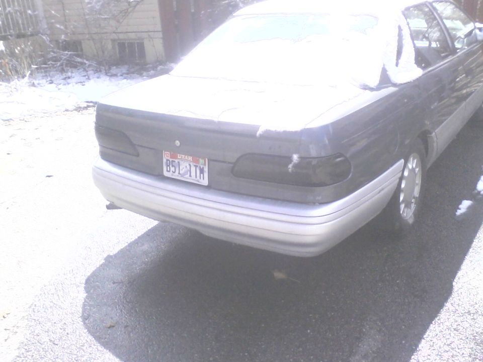 Rear of a dark gray sedan with Utah plate parked on pavement near snow