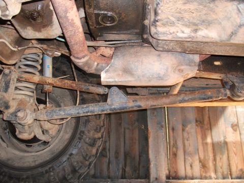 1996 Ford Bronco - The underside of a vehicle reveals its suspension, exhaust, and transmission components, with visible rust and a Ford emblem.