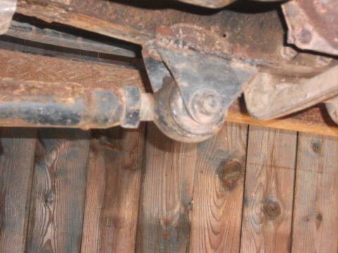 1996 Ford Bronco - Close-up view of a rusty vehicle suspension part against a wooden wall.