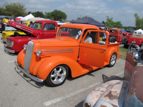2006 BMW 5 Series - Custom orange pickup truck displayed at an outdoor car show with other vehicles.