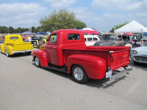 2006 BMW 5 Series - A red classic pickup truck is parked at an outdoor event with other vehicles and tents visible.