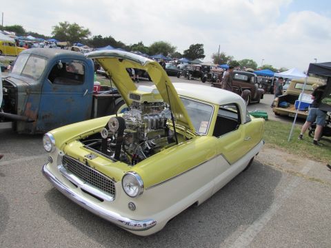 2006 BMW 5 Series - A custom Nash Metropolitan with its hood open, revealing a powerful engine, parked at an outdoor car show.