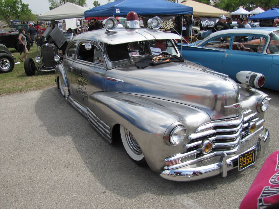 Chrome police car with siren and lights, parked at an outdoor event with other vehicles