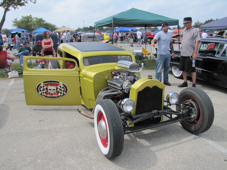 Yellow hot rod with open door, skull and checkered flag decal, exposed engine, and white-wall tires