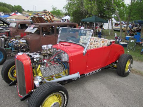 2006 BMW 5 Series - A bright red hot rod roadster is parked next to a rusty vintage car at an outdoor event.