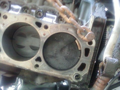1990 Ford Bronco - Close-up of an engine block's cylinders and pistons, with a rusty chain attached.