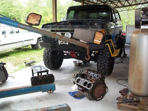 1990 Ford Bronco - This lifted 1990 Ford Bronco is undergoing engine work, with the engine block and cylinder head visible nearby.