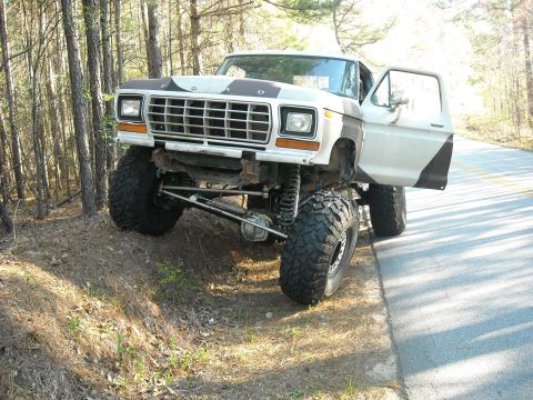 1979 Ford F-150 - Modified 1979 Ford F-150 truck with off-road tires sits on a dirt embankment next to a paved road.