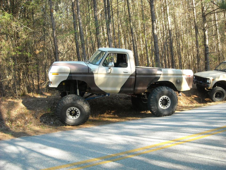 Lifted pickup truck with camouflage paint parked on the side of a road next to another truck