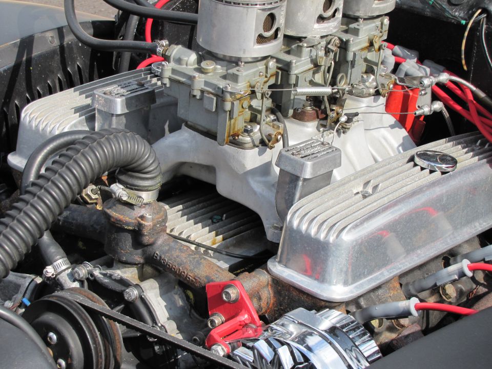 Close-up of a V8 engine with dual carburetors, aluminum valve covers, and red spark plug wires