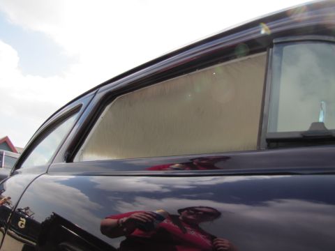 2006 BMW 5 Series - Side view of a dark sedan with a sunshade on the rear window, reflecting a person holding a bottle.